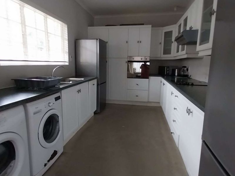 Functional kitchen featuring white cabinetry, dark countertops, integrated oven, extractor fan, and dedicated space for laundry appliances under the counter.