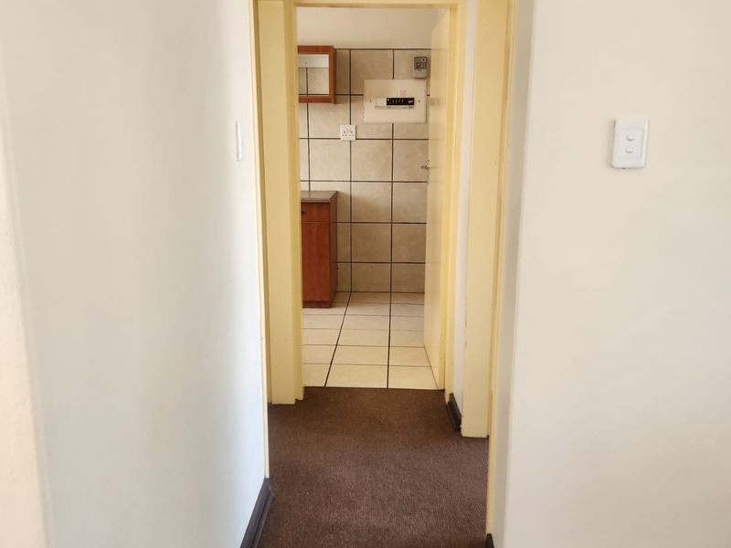 A functional hallway connecting to a tiled utility or kitchen area, featuring neutral walls and a combination of carpet and tile flooring.