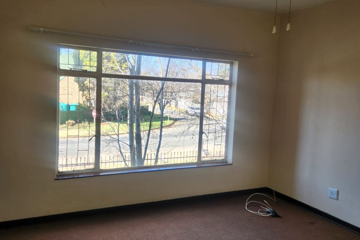 An empty bedroom featuring carpet flooring, a ceiling fan, and a large window with security bars overlooking the street.