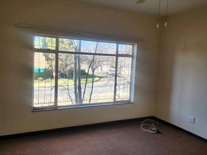 An empty bedroom featuring carpet flooring, a ceiling fan, and a large window with security bars overlooking the street.