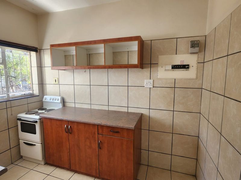 A compact kitchen area featuring basic wooden cabinetry, a laminate countertop, a freestanding stove, and full-height wall tiling.