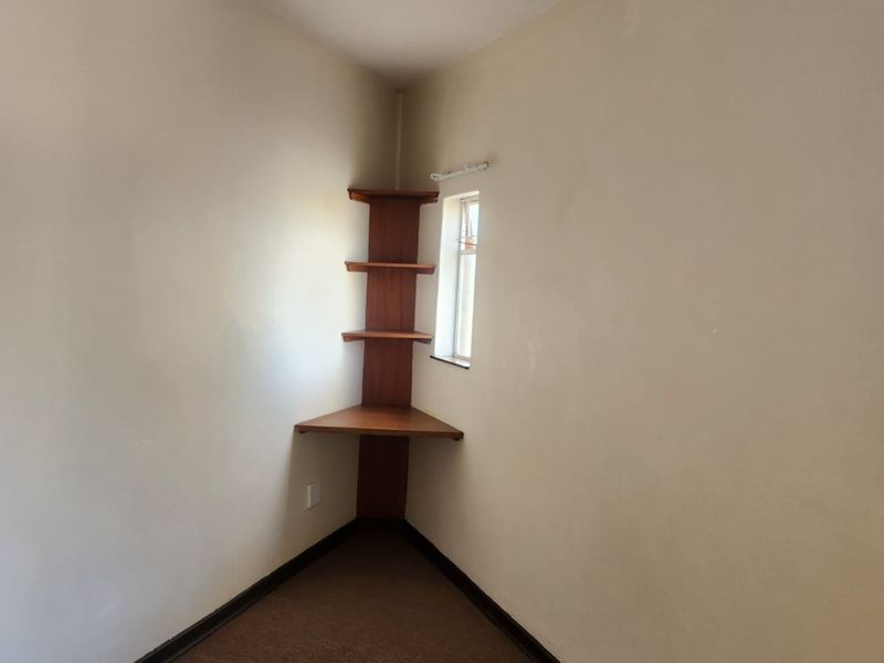 An empty bedroom corner featuring built-in wooden shelving, carpeted flooring, and a small window, offering a blank canvas for potential interior updates.