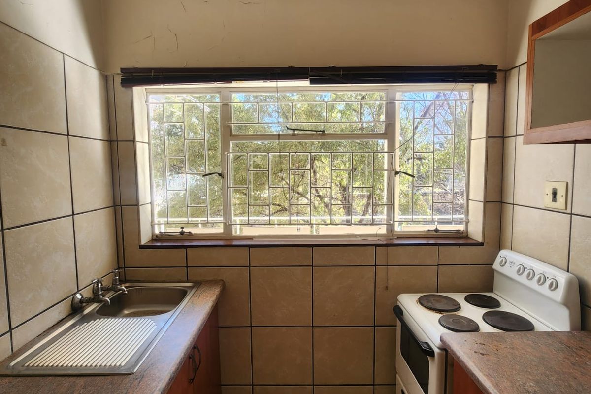 A compact kitchen featuring stone countertops, a stainless steel sink, and a freestanding stove, with tiled finishes and security bars on the window.