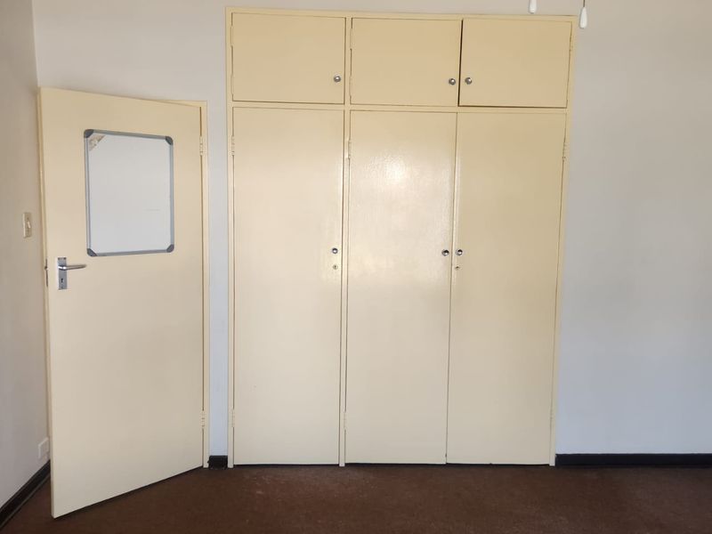 A vacant bedroom featuring built-in cupboards with overhead storage and carpeted flooring, offering a neutral space ready for personalization.