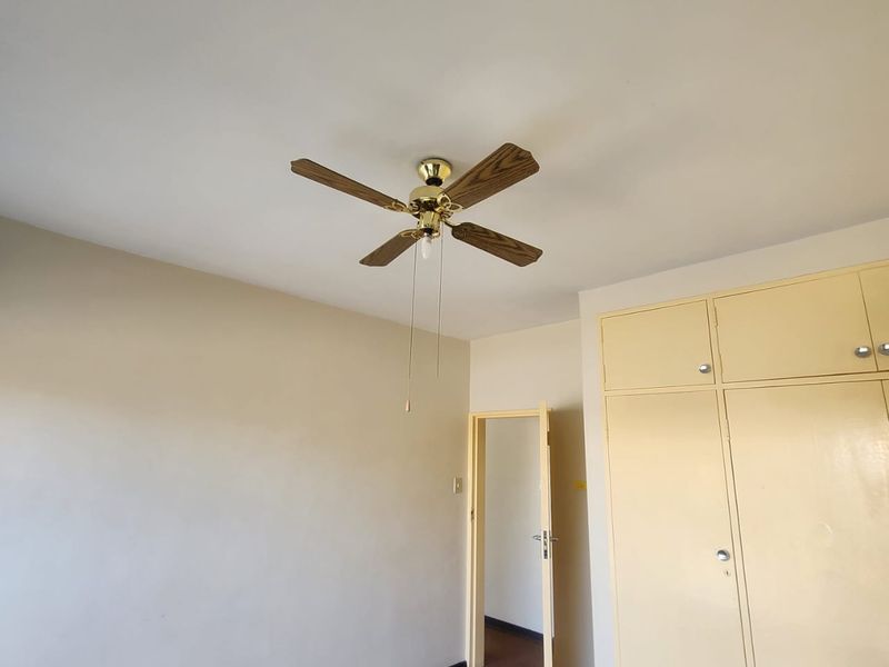 An empty bedroom featuring a ceiling fan and built-in cupboards, offering a blank canvas for renovation and interior design updates.