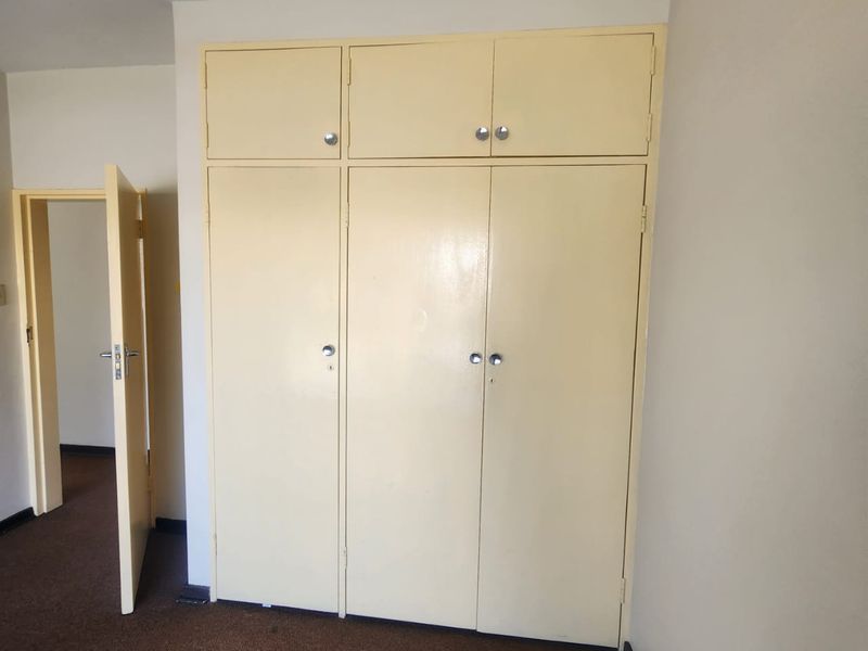 A bedroom featuring built-in cupboards with overhead storage and carpeted flooring, presenting a dated aesthetic suitable for modernization.