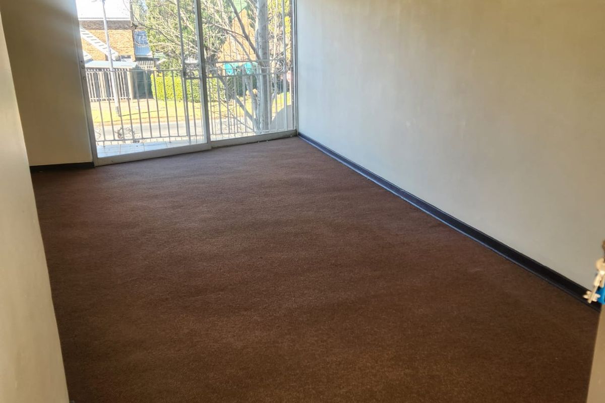 An empty living room featuring brown carpet flooring, a ceiling fan, and a large sliding glass door providing access to an outdoor balcony area.