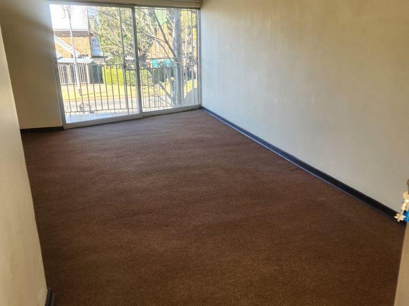 An empty living room featuring brown carpet flooring, a ceiling fan, and a large sliding glass door providing access to an outdoor balcony area.
