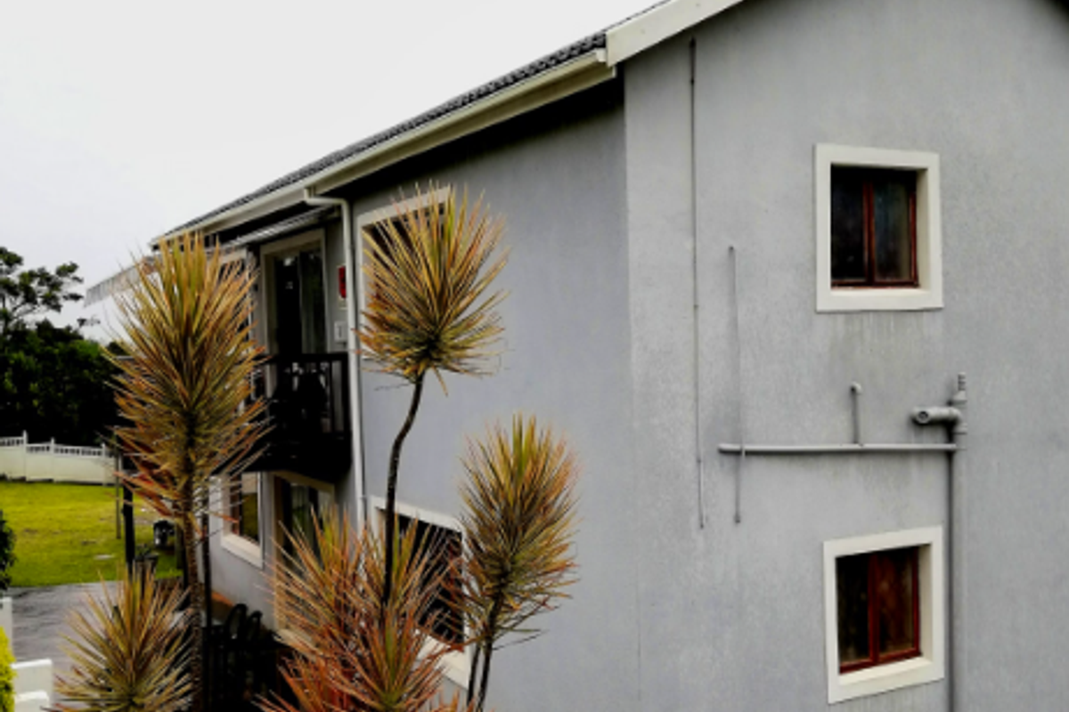 A side view of a two-story residential house featuring grey rendered walls, a pitched roof, and a small balcony.