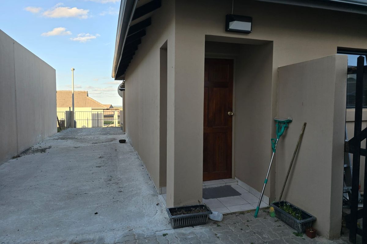 A side exterior view showing a concrete driveway, a paved walkway, and a timber entrance door with an external wall light.