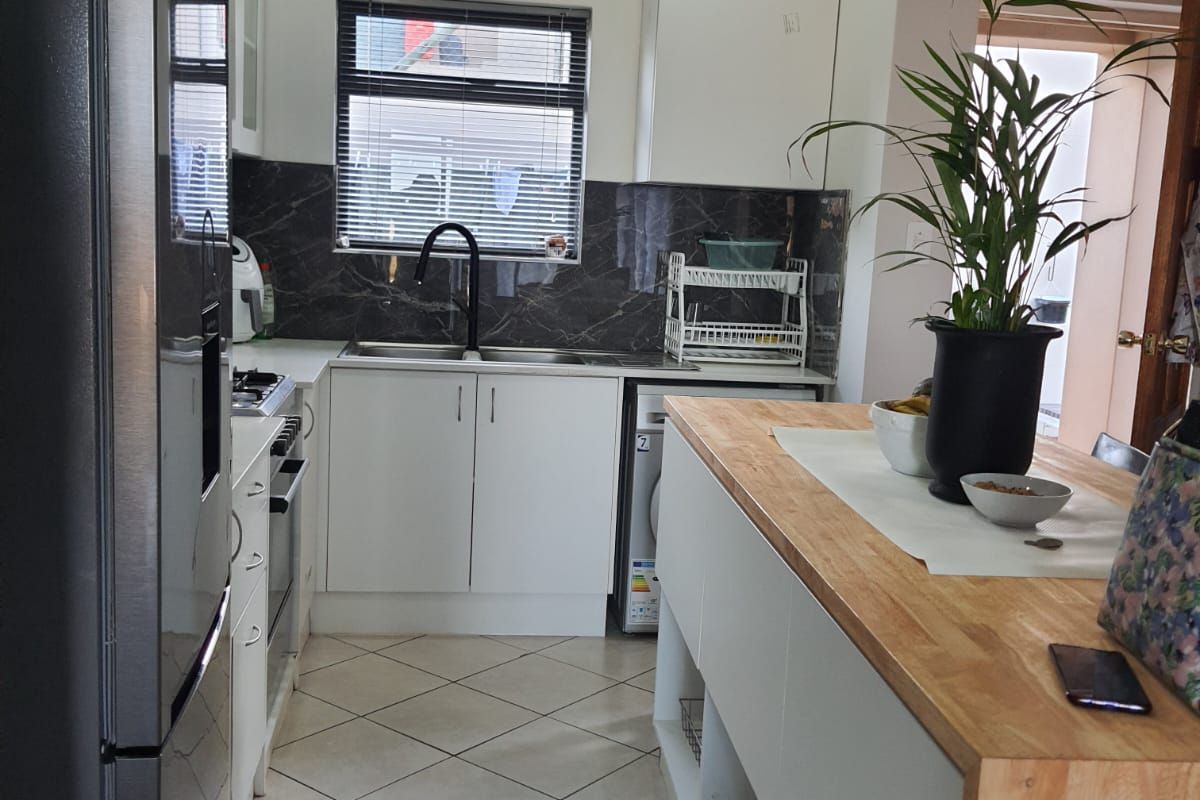 Modern kitchen featuring white cabinetry, a timber-topped island, stone-look splashback, and tiled flooring, offering a functional and clean workspace.