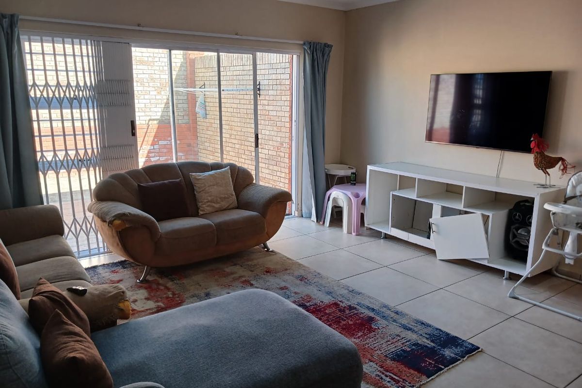 A living room featuring large sliding glass doors with security gates, tiled flooring, and a wall-mounted television area.