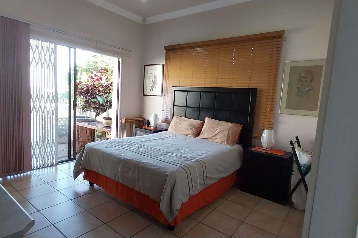 Spacious bedroom featuring tiled flooring, wooden blinds, and a sliding glass door providing direct access to an outdoor patio area.