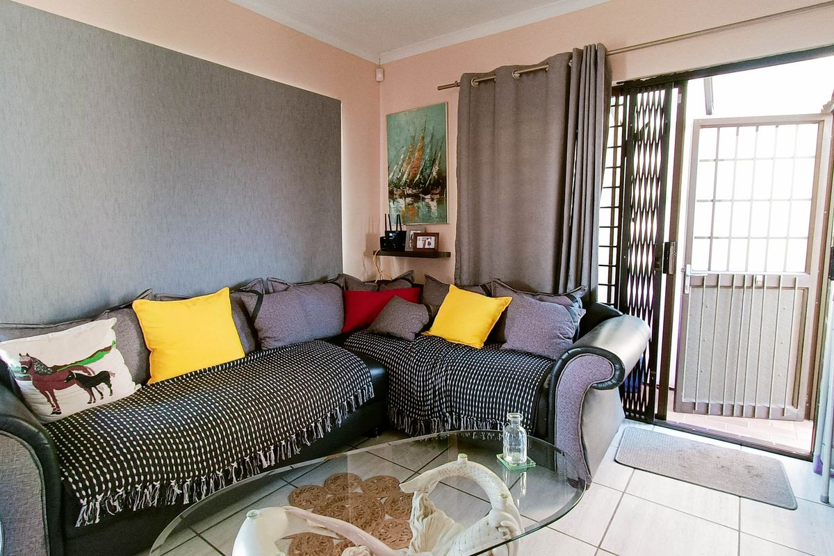 A living room featuring tiled flooring, an accent wall, and a sliding glass door with a security gate leading to the exterior.