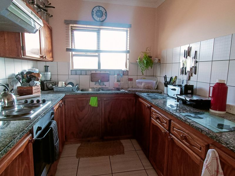 A functional U-shaped kitchen featuring granite countertops, wooden cabinetry, a double basin sink, and built-in cooking appliances with tiled finishes.