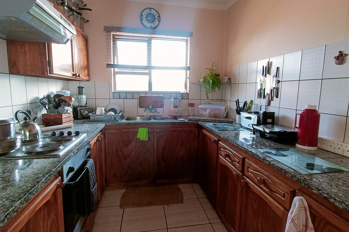 A functional U-shaped kitchen featuring granite countertops, wooden cabinetry, a double basin sink, and built-in cooking appliances with tiled finishes.