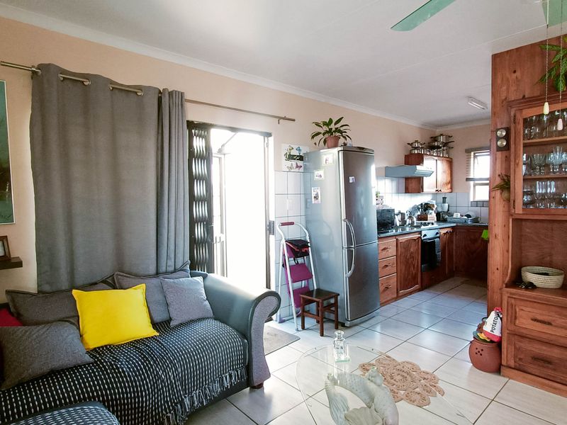 Open-plan living area featuring tiled floors, a functional kitchen with wooden cabinetry, and direct access to an outdoor space via a security gate.