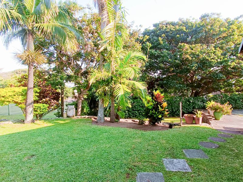 A well-maintained private garden featuring a lush green lawn, mature trees, and stone stepping stones leading along the side of the townhouse.
