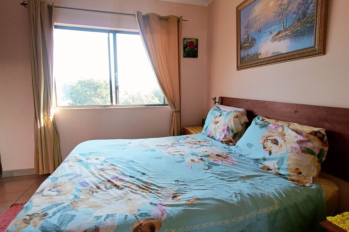 A functional bedroom featuring tiled flooring, a built-in wardrobe, and a large sliding window providing natural light.