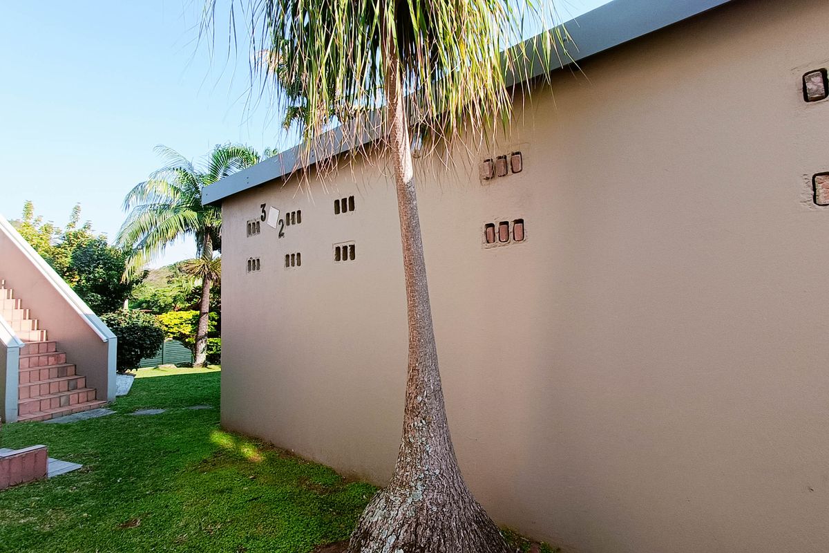 Rear exterior view of the townhouse featuring a concrete staircase, plastered walls with ventilation blocks, and a well-maintained garden area.