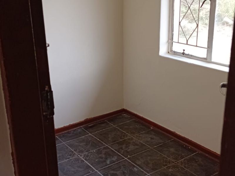 A small, empty room featuring dark tiled flooring, neutral walls, and a window fitted with security bars.