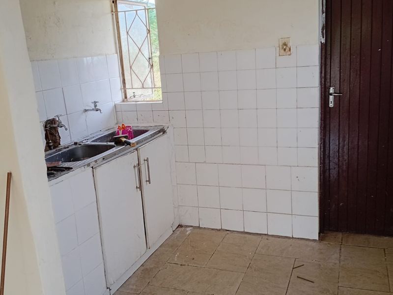 A functional, empty kitchen featuring a stainless steel sink, tiled splashback, and tiled flooring, ready for renovation or modernization.