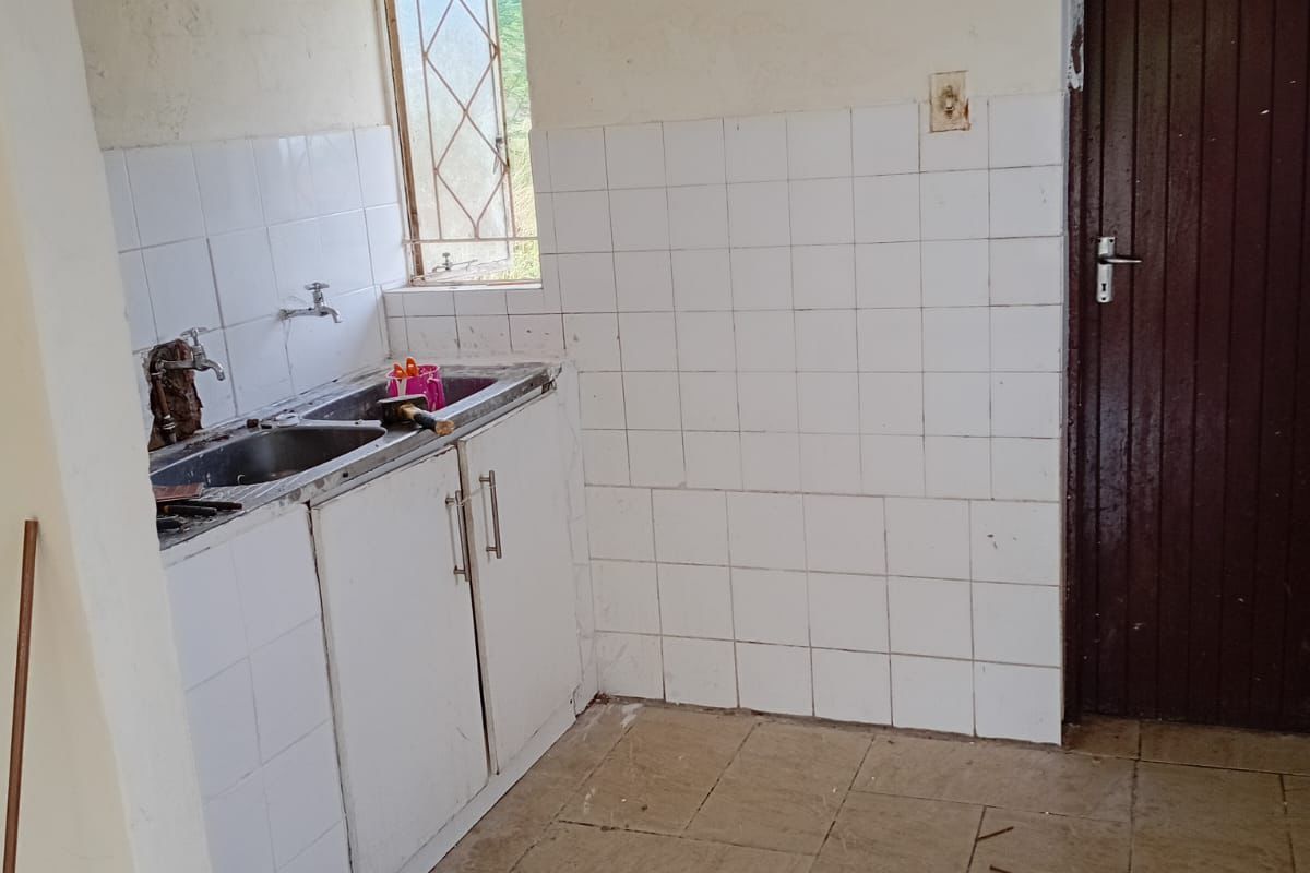 A functional, empty kitchen featuring a stainless steel sink, tiled splashback, and tiled flooring, ready for renovation or modernization.
