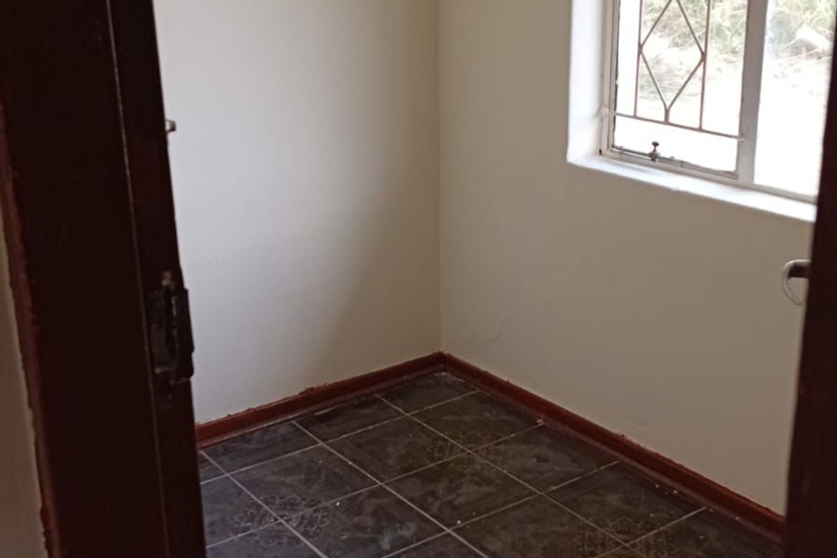 A small, empty room featuring dark tiled flooring, neutral walls, and a window fitted with security bars.