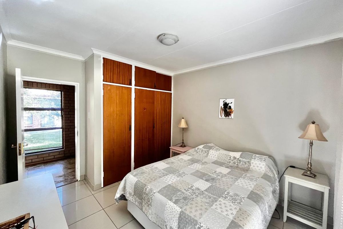 A bedroom featuring built-in wooden cupboards, tiled flooring, and a doorway leading to an adjacent space.