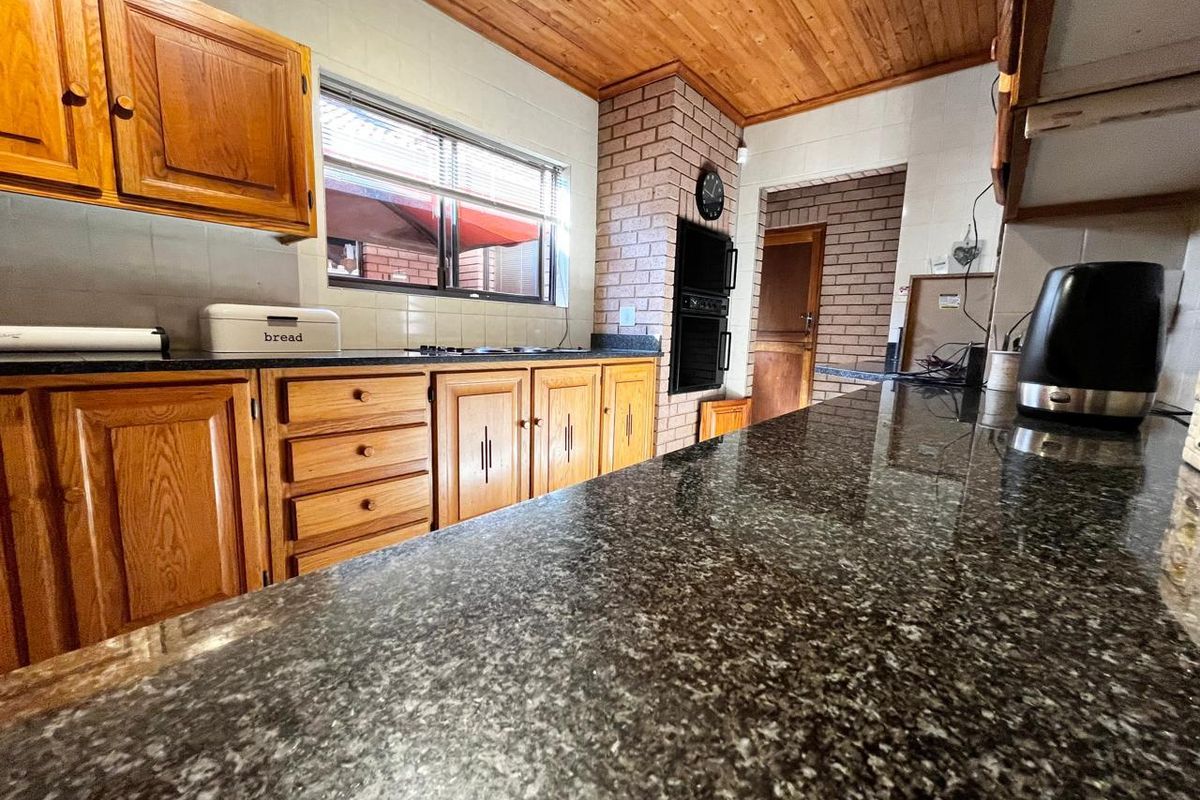 A functional kitchen featuring dark granite countertops, wooden cabinetry, a built-in oven, and a distinctive brick feature wall with a timber-paneled ceiling.
