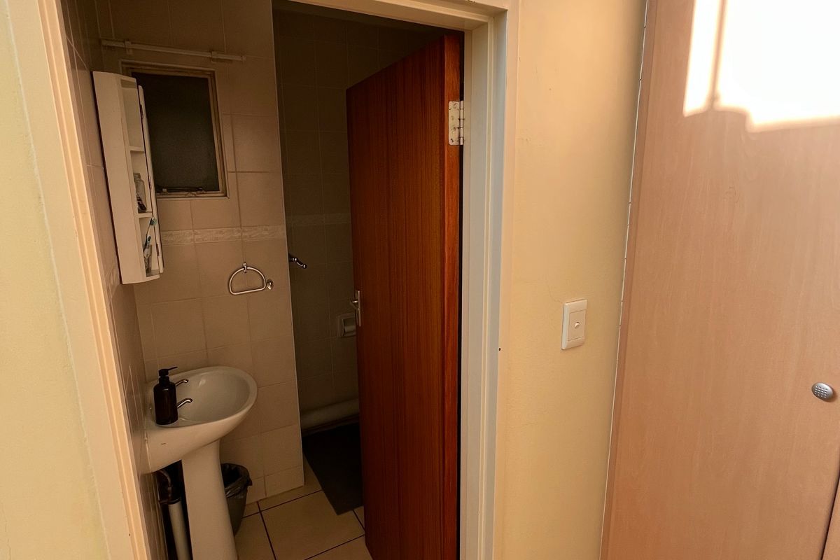 A functional bathroom featuring a pedestal basin, tiled flooring, and a built-in cupboard for storage.