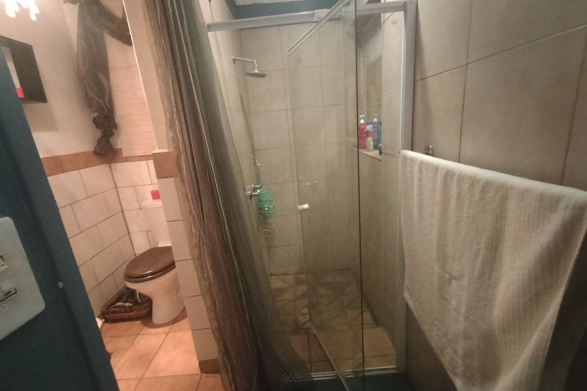 A functional bathroom featuring a glass-enclosed shower, tiled walls, and a standard toilet, presenting a dated but practical layout.
