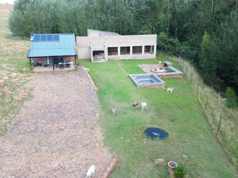 Aerial view of a farm property featuring a main dwelling with solar panels, an unfinished brick structure, a plunge pool, and a stone driveway.