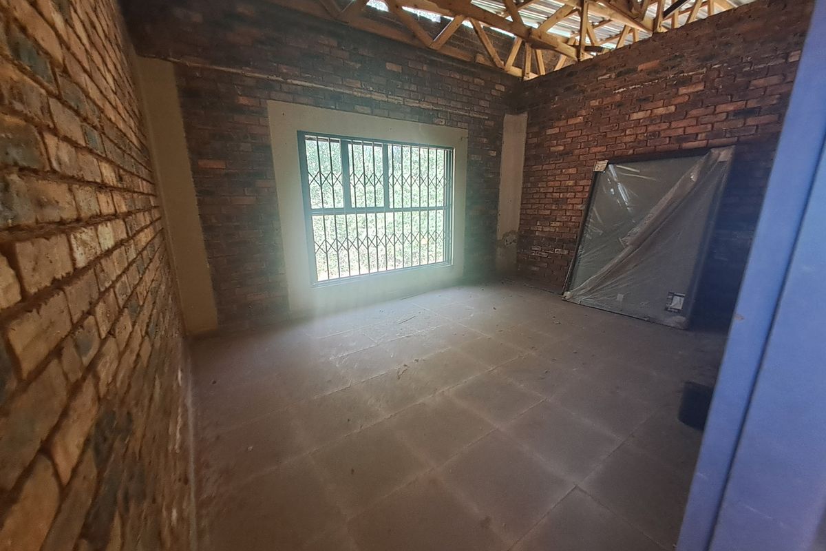 An unfinished bedroom space featuring exposed brick walls, tiled flooring, and visible timber roof trusses, awaiting final interior finishes and ceiling installation.