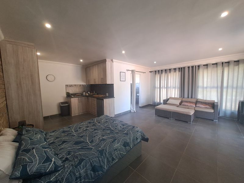 An open-plan studio space featuring a compact kitchenette with built-in cabinetry, tiled flooring, and recessed lighting, offering a functional living and sleeping area.