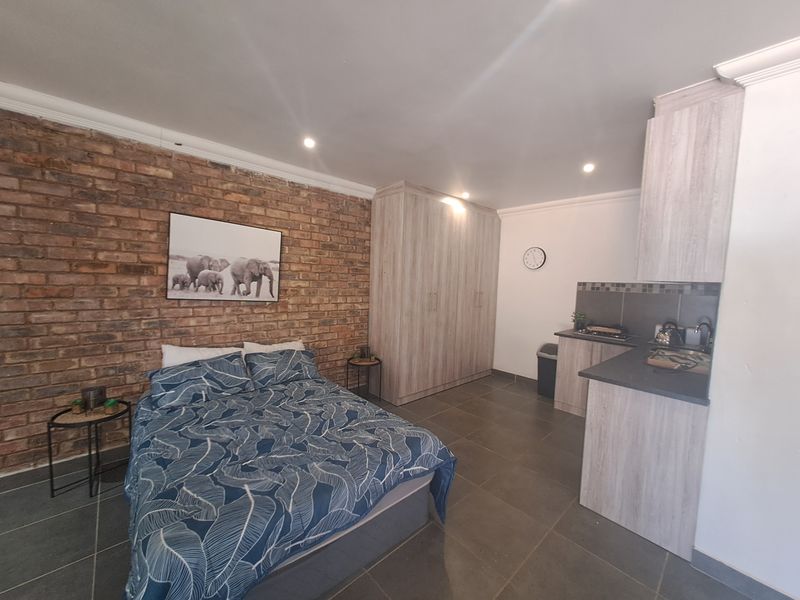 An open-plan studio space featuring an exposed brick feature wall, built-in storage cupboards, and a compact kitchenette with modern cabinetry and tiled finishes.
