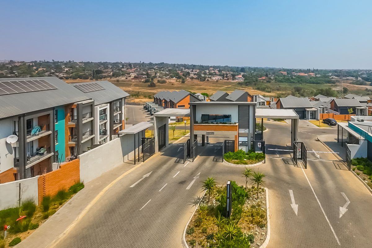 Aerial view of the townhouse complex entrance, featuring a secure gatehouse, paved access roads, and modern residential units with solar panels.