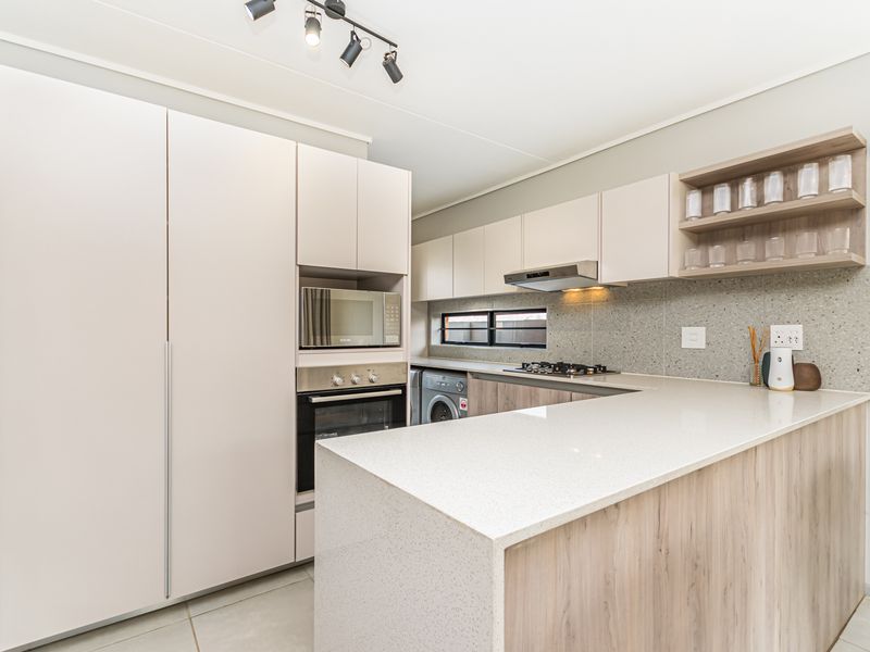 Modern kitchen featuring light wood-tone cabinetry, stone countertops, integrated appliances, and a gas hob with an extractor fan.