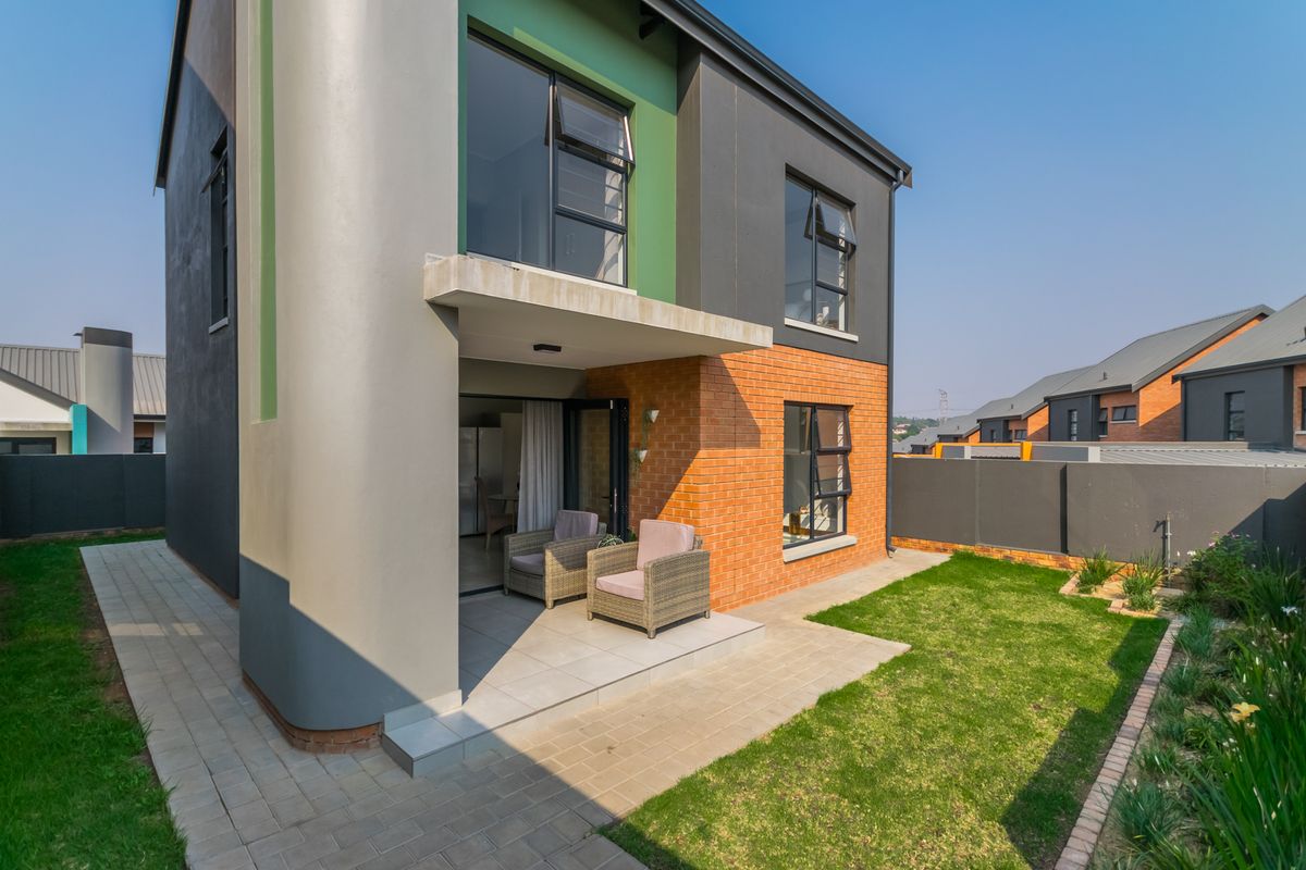 Rear view of a modern townhouse featuring a covered patio, brick and plaster facade, aluminium windows, and a private garden with a paved walkway.