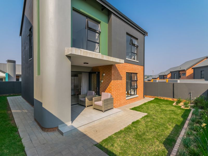 Rear view of a modern townhouse featuring a covered patio, brick and plaster facade, aluminium windows, and a private garden with a paved walkway.