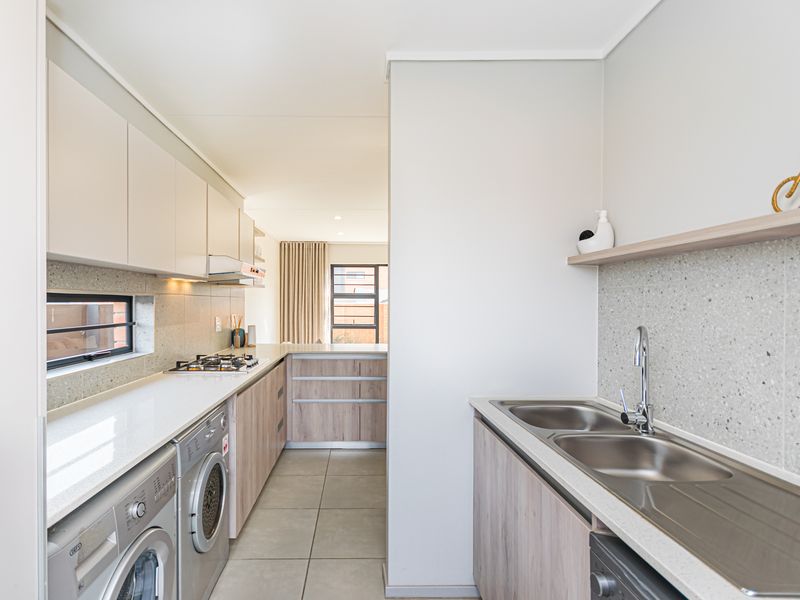 Modern scullery featuring sleek cabinetry, stone countertops, a double stainless steel sink, and a built-in gas hob with an extractor fan.