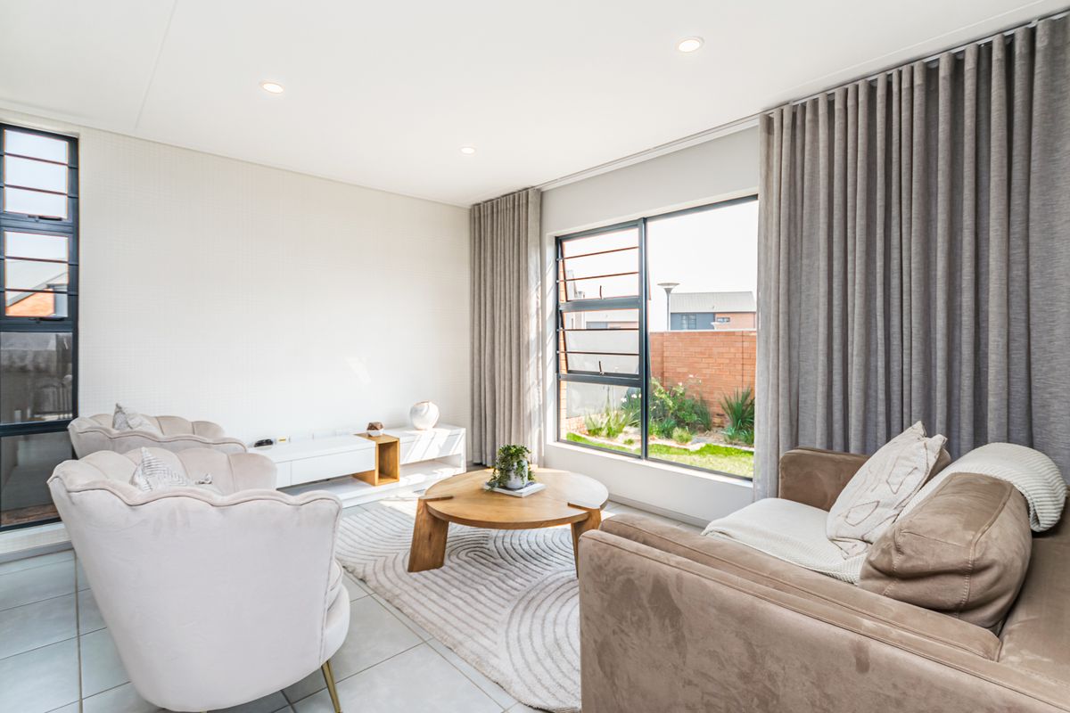 A bright and modern living room featuring large aluminium windows, tiled flooring, and recessed downlighting, offering a clean and well-maintained living space.