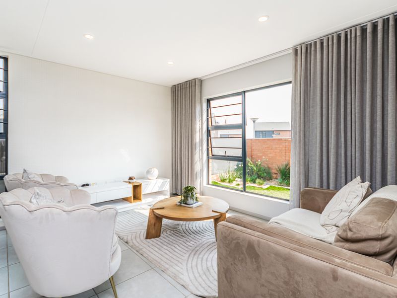 A bright and modern living room featuring large aluminium windows, tiled flooring, and recessed downlighting, offering a clean and well-maintained living space.