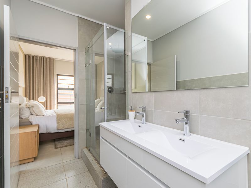 Modern bathroom featuring a double vanity with integrated sinks, a glass-enclosed shower with a rain shower head, and neutral wall and floor tiling.