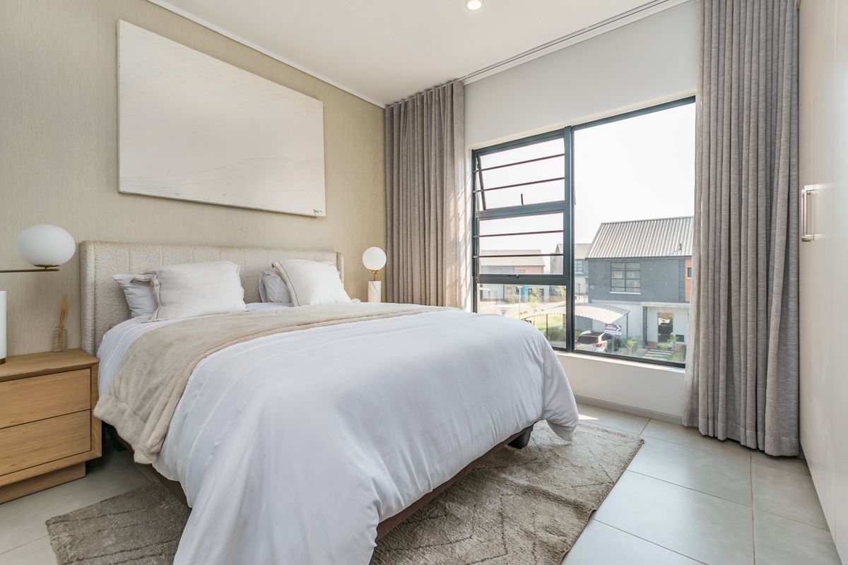 A bright and modern bedroom featuring large windows, neutral tiled flooring, and a built-in wardrobe, offering a clean and contemporary living space.