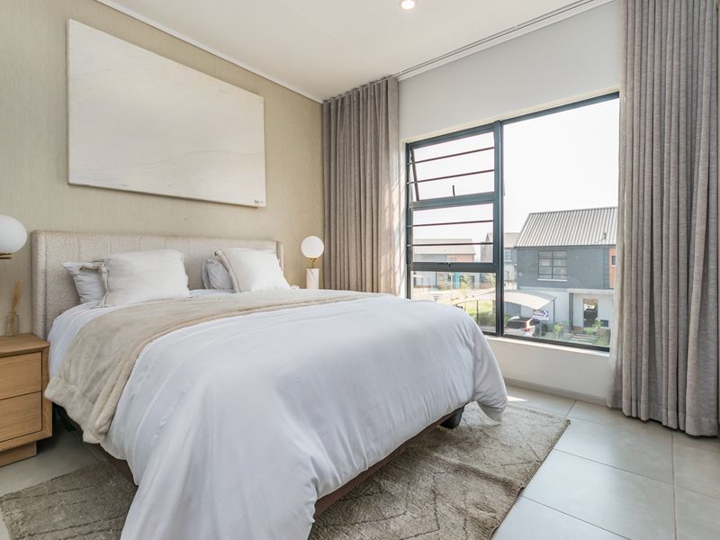 A bright and modern bedroom featuring large windows, neutral tiled flooring, and a built-in wardrobe, offering a clean and contemporary living space.