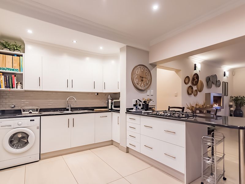 Modern open-plan kitchen featuring white cabinetry, stone countertops, a gas hob, and an integrated washing machine, flowing seamlessly into the adjacent living area.
