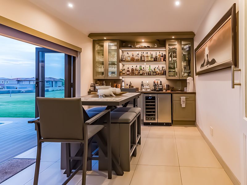 A sophisticated built-in home bar featuring custom cabinetry, integrated wine refrigeration, glass display shelving, and seamless access to the outdoor patio area.