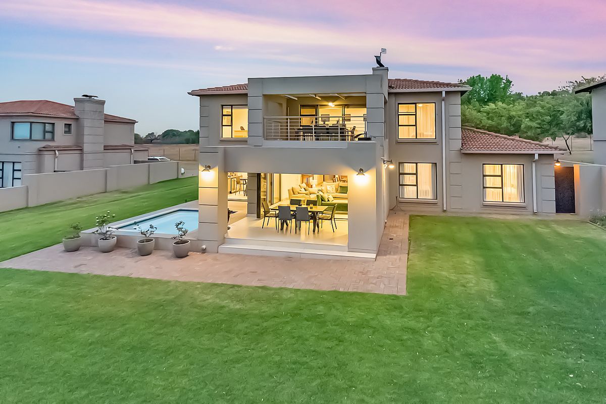 Rear view of a modern two-story house featuring a swimming pool, covered patio, and an upper-level balcony set within a landscaped garden.