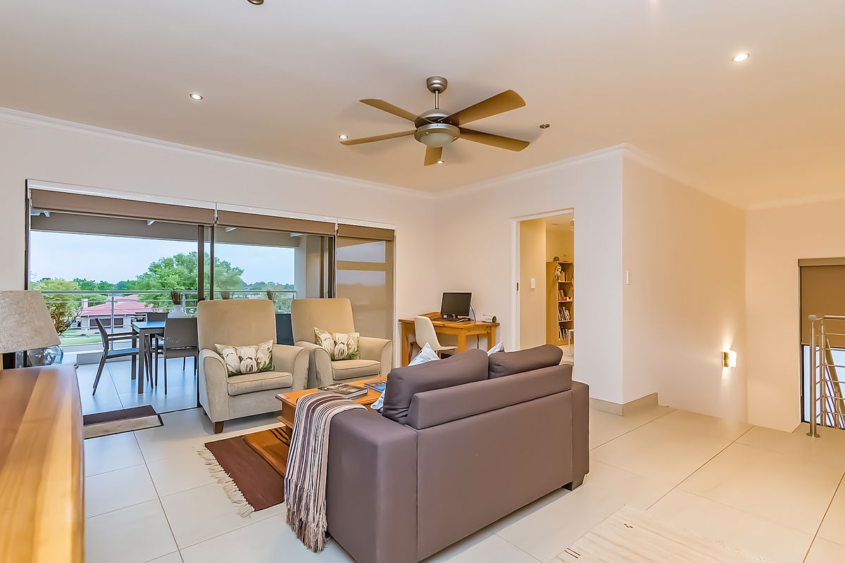 A bright and spacious living room featuring large sliding glass doors that open onto a balcony, tiled flooring, and a modern ceiling fan.